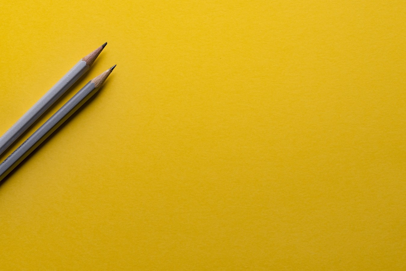 Two gray pencils on a bright yellow background